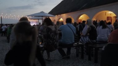 İnsanlar yerel konser için bahçede masalarda oturuyorlar. Sıcak bir atmosfer. Yaz gecesi. 1080p.