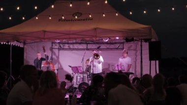 Seyirci kafalar üzerinde küçük bir açık hava konserinin geniş açısını çekiyoruz. Çift bas, trombon, davul, anahtar. 1080p.