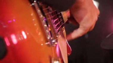 Sahnede turuncu elektro gitar çalan müzisyen elinin yakın çekimi..