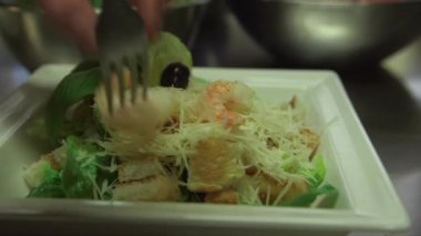 Ceasar salatasına karides tozu atılıyor. Kadın aşçı elleri çatalla hızlı çalışıyor.