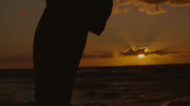 Gün batımında deniz kenarında duran siluette kadının bacaklarının yakın çekim görüntüsü, 4k, yavaş çekim.
