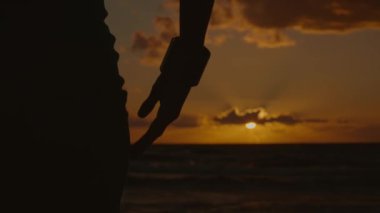 Gün batımında deniz kenarında dans eden bir kadının siluetinin yakın çekim görüntüsü, 4K, yavaş çekim.