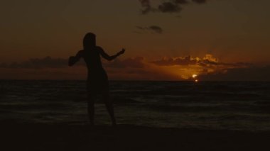 Silüet içinde, güneşin battığı arka planda dans eden bir kadının durgun geniş açılı görüntüsü, 4K, yavaş çekim.