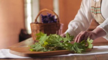 Geleneksel kostüm giymiş bir kadının ahşap bir tahtanın üzerinde akçaağaç yaprakları düzenlerken çekilmiş statik görüntüsü.