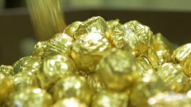 statik yavaş çekim makro şekerler altın renkli folyolar içinde çikolata fabrikasında büyük bir yığının içine düşüyorlar.