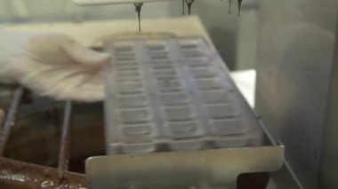 Bir çikolata fabrikasında kalıbı sıvı çikolatayla dolduran bir pasta şefinin statik yavaş çekimi.