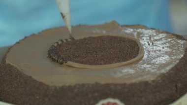 Hamur işi şefinin kahverengi bir pastaya krem şanti sürerken çekilen yavaş çekim makro görüntüsü.