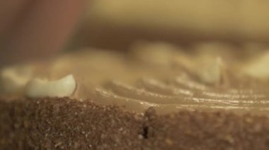 Hamur işi şefinin kahverengi bir pastaya krem şanti sürerken çekilen yavaş çekim makro görüntüsü.