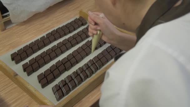 Долли Замедленной Съемки Среднего Снимка Кондитера Украшающего Квадратный Шоколад Белым — стоковое видео