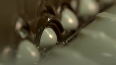 durağan ağır çekim makro beyaz şekerlemelerin konveyör hattında sıvı çikolatayla kaplanması.