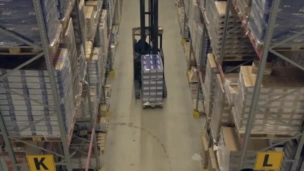 倉庫の棚の間で働くリーチトラックの広いショットの後にパンアップ — ストック動画