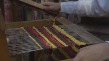 Geleneksel tişörtlü bir çocuğun dokuma tezgahıyla renkli bir bez battaniye örerken yakın plan çekimleri.