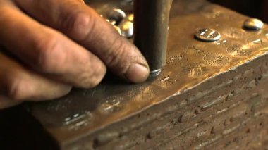 Demirci antika bir yazı sembolünü yuvarlak bir metal parçasına çarpıyor. Demirci, öncelikle Demir ya da Çelik 'ten ama bazen de diğer metallerden nesneler yaratan bir demircidir..