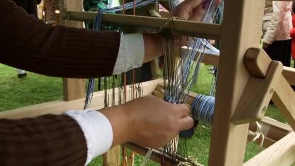 女性は ルームで織る準備をしています アイレットを通してスレッドを配置します 織り方は織物や布を形作るために2セットのヤーンを交換する織物の生産方法です — ストック動画