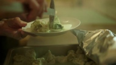 Elinde Slotted Spoon olan bir kadın Sovyet-Dönem kantinindeki bir tabağa hamur tatlısı koyar. 80 'lerin Stili Öğle Yemeği - Yağlı bezle kaplı Masalarda Kesik Cam Bardaklardan İçme.