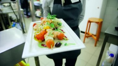 Dikdörtgen bir tabakta gurme yemeği. Garson kız onu salona getiriyor. Mutfaktan restorana doğru yürü. Ağız sulandıran Harika Yemek Manzarası.