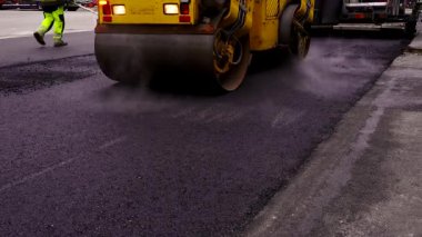Asfalt Paving. Road Roller Sıcak, Buharlı, Taze Asfalt Üzerinde Sürüyor. Road Roller, Paten sıkıştırıcı veya paten sıkıştırıcı, asfalt sıkıştırmak için kullanılan bir sıkıştırma tipi mühendislik aracıdır..