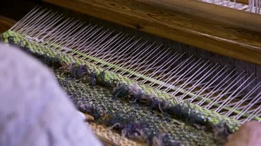Geniş dokuması olan yaşlı bir kadın renkli, dekoratif bir duvar halısı ya da halısı dokuyor. Dokuma bir tekstil üretim metodudur. Bir kumaş veya kumaş oluşturmak için iki iplik dizisi birbirine karışır..