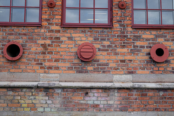 Ventilation pipes and vents coming out of a brick facade.