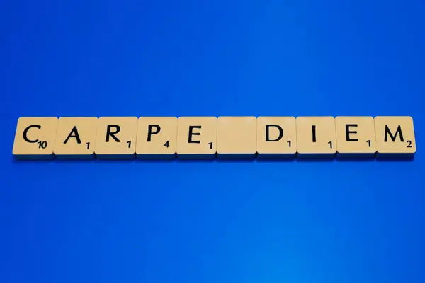 Mavi arka planda Scrabble harfleri olan Carpe Diem tabelası.