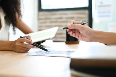 İki kişi bir kağıt parçasına yazı yazıyor. Bir tanesi kalem tutuyor, diğeri de kalem tutuyor..