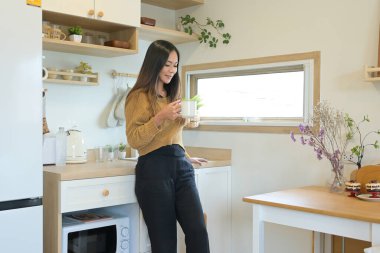 Bir kadın mutfakta elinde bir fincan kahve tutuyor..