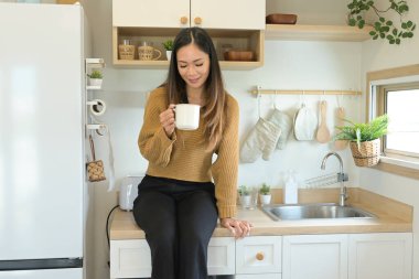 Bir kadın mutfak tezgahında elinde bir fincan kahveyle oturuyor..