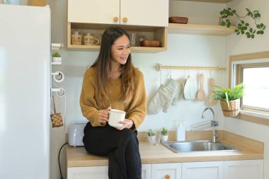 Bir kadın mutfak tezgahında elinde bir fincan kahveyle oturuyor...