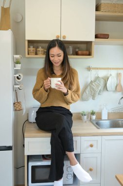 Bir kadın mutfak tezgahında elinde bir fincan kahveyle oturuyor...