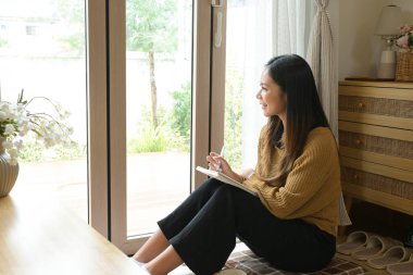 Önünde bir not defteriyle yerde oturan bir kadın. Gülümsüyor ve eğleniyor..