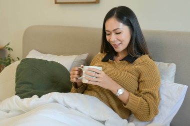 Bir kadın elinde bir fincan kahveyle yatakta oturuyor...