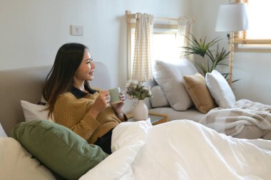 Bir kadın elinde bir fincan kahveyle yatakta oturuyor...