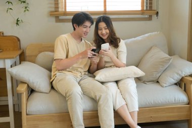 Bir adam ve bir kadın koltukta oturuyor, ikisi de cep telefonlarına bakıyor..