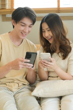 Bir adam ve bir kadın koltukta oturuyor, ikisi de cep telefonlarına bakıyor...