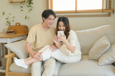 Bir adam ve bir kadın koltukta oturuyor, ikisi de cep telefonlarına bakıyor...