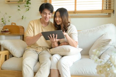 Bir adam ve bir kadın kanepede oturmuş tablete bakıyorlar. Gülümsüyorlar ve birlikte iyi vakit geçiriyorlar...