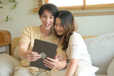 Bir adam ve bir kadın kanepede oturmuş tablete bakıyorlar. Gülümsüyorlar ve birlikte iyi vakit geçiriyorlar...