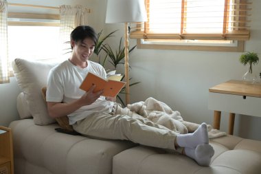 Bir adam kanepede kitap okuyor. Gülümsüyor ve eğleniyor..