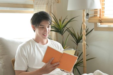 Bir adam kanepede kitap okuyor. Gülümsüyor ve eğleniyor...