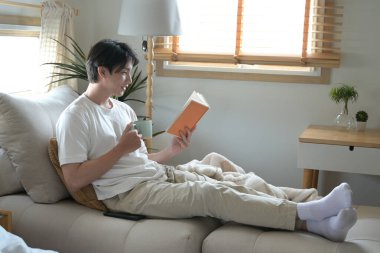 Bir adam elinde bir fincan kahve tutarken kitap okuyor..