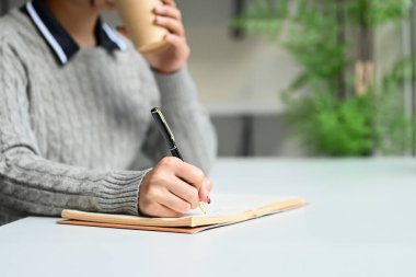 Bir kadın elinde kahve tutarken deftere bir şeyler yazıyor...