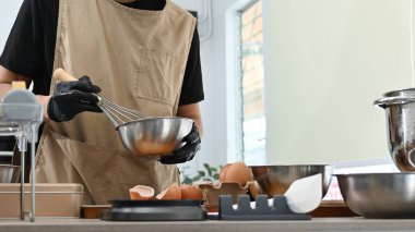 Bir adam mutfakta bir pasta yapıyor. Önlük ve eldiven giyiyor. Tezgahta birkaç kase ve kaşık var...