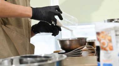 Mutfakta bir kişi tatlı yapıyor. Eldiven takıyor ve bir kaseye beyaz toz döküyor..