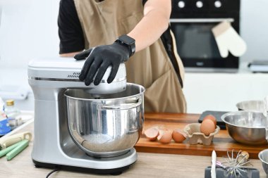 Mutfakta bir kişi pasta yapıyor. Siyah önlük ve eldiven giyiyor. Pasta hamuru önce karıştırma kabına sonra da miksere dökülüyor...
