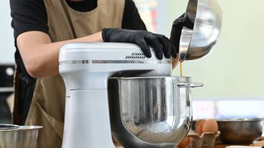 Mutfakta bir kişi pasta yapıyor. Siyah önlük ve eldiven giyiyor. Pasta hamuru önce karıştırma kabına sonra da miksere dökülüyor..