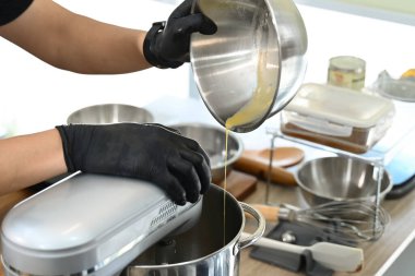 Mutfakta bir kişi pasta yapıyor. Siyah önlük ve eldiven giyiyor. Pasta hamuru önce karıştırma kabına sonra da miksere dökülüyor...