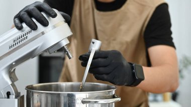 Bir adam mutfakta mikseri tamir ediyor. Siyah eldiven ve kahverengi önlük giyiyor...