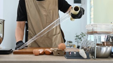 Bir adam yumurtaları naylona sarıyordu. Yumurtalar ahşap bir kesme tahtasının üzerinde. Adam önlük ve eldiven giyiyor...