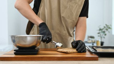 Bir adam kurabiye bıçağıyla kurabiye hamuru yapıyor. Eldiven ve önlük giyiyor..