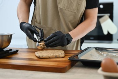 Bir adam kurabiye bıçağıyla kurabiye hamuru yapıyor. Eldiven ve önlük giyiyor...